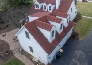 Aerial view of residential home with red shingle roof, dormer windows, and driveway, showcasing durable roofing and well-maintained exterior.