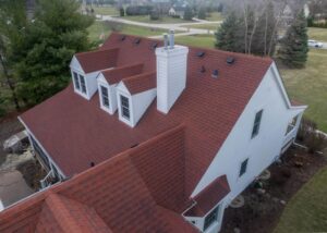 Aerial view of a residential home with red shingle roofing, dormers, and chimney, highlighting durable materials and well-maintained roofing system.