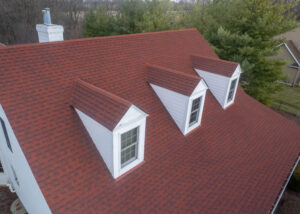 Close-up of residential roof with red asphalt shingles and dormer windows, highlighting durable materials and clean, well-maintained roofing design.