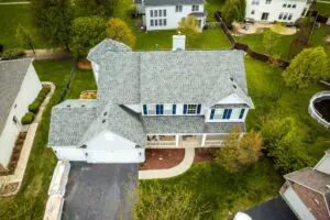 Aerial view of a well-maintained suburban home with fresh roofing, clean driveway, and landscaped yard showcasing improved curb appeal and exterior design.
